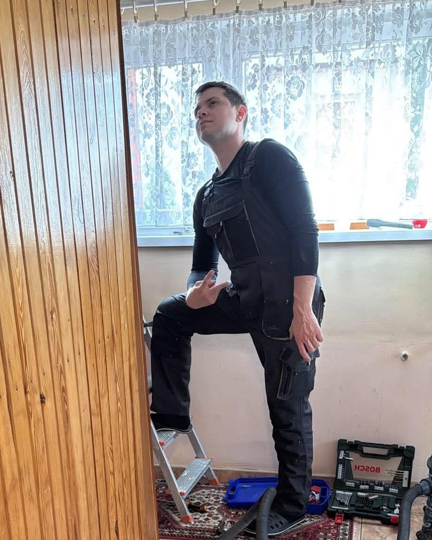 Bartosz w roboczym kombinezonie, z nogą na drabinie, patrzy w górę