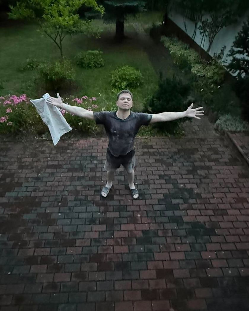 Bartosz na podwórku z rozłożonymi rękami i ścierką w dłoni